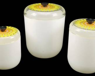 1202 - 3pc Vtg Acrylic Canister Set w/ Sunflower (Description): A three-piece vintage acrylic canister set  featuring frosted white bodies with clear  lids decorated with bright yellow and orange  sunflower designs. Each lid has a dark brown  knob finial. The set includes three graduated sizes. Largest measures 6.5"x 5".