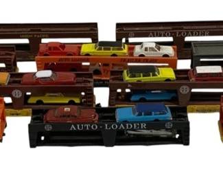 1607 - 10pc Lot HO Scale Car Carrier Train Cars (Description): A collection of ten HO scale car carrier  train cars. The lot includes various  auto-loader flatcars in brown, black, and  orange liveries, featuring brands such as  Santa Fe and Trailer Train. Each carrier is loaded with miniature die-cast automobiles in  assorted colors including yellow, red,  white, and blue. The collection represents  vintage toy train accessories suitable for  model railroad layouts.