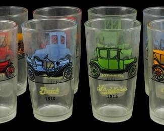 1018 - 8 Vintage Automobile Collectible Glasses (Description): Set of eight vintage collectible drinking  glasses featuring colorful depictions of  early automobiles. Each glass displays a  different classic car with its manufacturer  name and year, including Stutz 1914, Buick 1910, Studebaker 1915, and Chevrolet 1913.  The detailed illustrations showcase the  distinctive styles of early 20th century  automobiles in vibrant colors including red,  blue, green, and orange against clear glass.