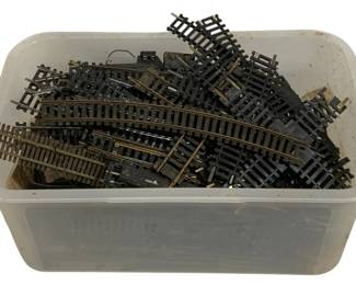 1589 - Plastic Tote Full of HO Scale Train Tracks (Description): A plastic tote filled with HO scale model  train tracks. The collection includes various  track sections featuring both straight and  curved pieces, as well as switches and  junction tracks. The tracks feature brass rails mounted on black plastic ties,typical  of HO gauge model railroad track systems.