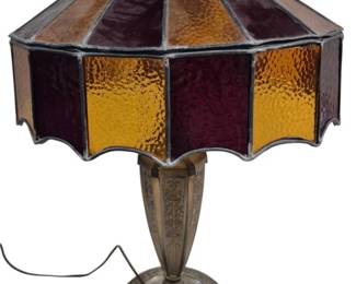 1434 - Vintage Stained Glass Lamp Some Panels Loose (Description): Vintage stained glass lamp featuring  alternating amber and purple or red textured  glass panels in a decorative shade with metal  framework. Some panels are loose. The lamp  stands on a decorative metal base with ornate detailing. Measures 24 inches tall. Used as  is electric/electronic/mechanical item. No  guarantee all components present, untested.