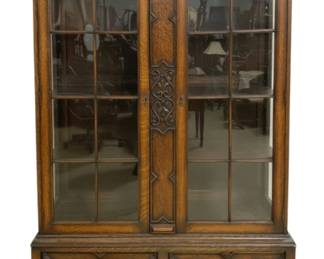 7782 - English Oak Barley Twist Two Door Carved Bookcase (Description): English oak two door bookcase featuring  carved foliate frieze along the crown, leaded  glass doors with decorative central stile,  and two drawers with brass drop pulls. The  case rests on distinctive barley twist legs connected by a matching stretcher. Measures  67" high x 44" wide x 15" deep.