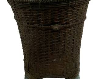1504 - Woven Basket Style Bronze Metal Planter (Description): A distinctive bronze metal planter crafted to  resemble a woven basket. The piece features  an intricate basketweave pattern throughout  the body with a braided rope detail around  the rim. Small decorative knob accents adorn the sides, and the planter rests on four  tapered feet. The surface displays a rich  brown patina with hints of verdigris,  suggesting age and character. Measures 10  inches by 9.5 inches.