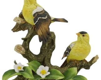 1076 - Angeline Hand Painted Japan Porcelain Bird (Description): Angeline hand painted porcelain bird figure  made in Japan. This charming figurine  features two yellow and black goldfinches  perched on a naturalistic tree branch with  white dogwood blossoms and green leaves at the base. One bird is positioned higherwith  its beak open as if singing, while the second  bird sits on a lower branch. The piece  showcases detailed hand-painted plumage and  realistic coloring. Measures 8 inches.