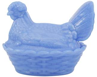 1043 - Blue Glass Hen on Nest Figure 5"x6"x4.5" (Description): Blue glass hen on nest figure. This charming  covered dish features a detailed hen sitting  atop a woven basket-style base. The piece is  crafted in opaque periwinkle blue milk glass  with intricate feather detailing on the hen's body and wings. Measures 5" x 6" x 4.5".
