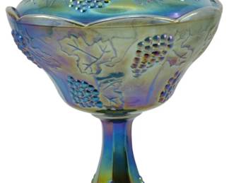 671 - Indiana Blue Harvest Grape Carnival Compote (Description): Vintage Indiana Blue Harvest Grape carnival  glass lidded compote. This iridescent piece  features a grape and leaf motif in relief  throughout the bowl, lid, and pedestal base.  The lid is topped with a grape cluster finial. The glass displays a beautiful  blue-green-purple iridescent finish  characteristic of carnival glass. Measures  10.5 inches tall.