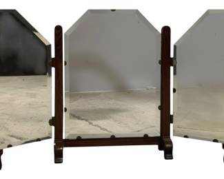 7788 - Vintage Mahogany Tri Fold Vanity Mirror (Description): Vintage trifold vanity mirror with a handsome  mahogany frame. The center panel features a  distinctive clipped-corner top design,  flanked by two hinged rectangular side panels  that fold inward for storage or adjust for optimal viewing angles. The mirror rests on a  sturdy base with turned supports and  decorative bun feet. Measures 28 inches by 42  inches when fully extended.