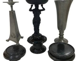 992 - Assorted Pewter, Metal & Black Glass Decor (Description): Assorted decorative items including a pewter  candlestick with pierced triangular base, a  neoclassical figural compote featuring a  draped female figure holding a swirled bowl  aloft, a pewter trumpet vase on turned base, a black glass column-form candleholder, and  several black lacquered wooden display bases  of varying sizes.