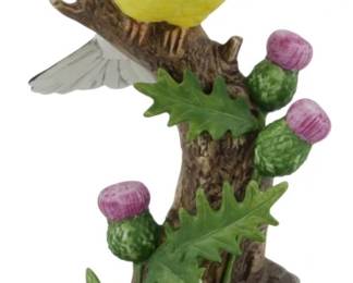 1079 - Andrea by Sadek Porcelain Gold Finch Figure (Description): Andrea by Sadek porcelain figure depicting a  gold finch perched on a branch with thistles.  The brightly colored yellow bird is shown  with wings spread, featuring gray and black  wing markings and an orange beak. The naturalistic base includes detailed green  thistle leaves and purple thistle blooms.  Measures 8.5 inches tall.