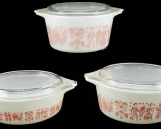 1039 - 3pc Pyrex Pink Butterprint Casserole Set (Description): Rare three-piece Pyrex Pink Butterprint  casserole set featuring the iconic  Amish-inspired pattern with roosters, corn,  and figures in pink on white milk glass. Each  covered casserole dish includes a clear glass lid with tab handles. The set includes  three graduated sizes, perfect for serving or  baking. Measurements: 3.5" x 7" x 6".