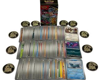 1568 - Lot of 300 Pokemon Cards w/ 2 Boxes & Coins (Description): A lot of 300 Pokemon cards accompanied by two  boxes, including a Chaos Rising booster  bundle box. The collection features various  card types with different colored borders  indicating different Pokemon types and rarities. Also included are several  collectible Pokemon coins featuring Chikorita  design in gold and black finish.