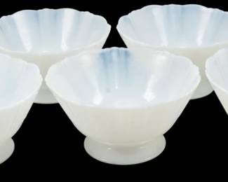 925 - 7 Monax American Sweetheart Sherbet Bowls (Description): Set of seven Monax American Sweetheart  sherbet bowls. These Depression-era glass  pieces feature the classic scalloped petal  rim design characteristic of the American  Sweetheart pattern. The translucent white opalescent Monax glass displays a subtle blue  tint toward the centers, with each bowl  resting on a circular pedestal foot. Measures  2.5 inches tall by 4.5 inches in diameter.