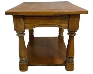 7658 - Oak End Table w/ Lower Shelf 26"x21"x21" (Description): Traditional oak end table featuring a solid  rectangular top with a single drawer beneath.  The table is supported by four turned legs  connected by a lower shelf for additional  storage or display. The piece showcases the natural grain of the oak woodwith a warm  honey-toned finish. Measures 26 inches by 21  inches by 21 inches.