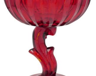 995 - Vtg Indiana Glass Ruby Red Pedestal Compote (Description): Vintage Indiana Glass ruby red pedestal  compote featuring a fluted tulip-shaped bowl  with a distinctive zigzag scalloped rim. The  compote sits on an elegantly curved stem with  a leaf-like design, resting on a circular footed base. This striking piece showcases  the rich, deep ruby red coloring  characteristic of Indiana Glass. Measures 7.5  inches by 6 inches.