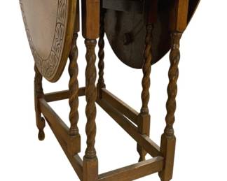 7768 - Vtg Oak Drop Leaf Gate Leg Table 28"x42"x29" (Description): Vintage oak drop leaf gate leg table  featuring distinctive barley twist turned  legs and stretcher base. The table displays  classic English styling with a warm oak  finish and oval-shaped top when extended. The gate leg mechanism allows the drop leaves to  fold down for compact storage. Measures 28  inches wide by 42 inches long by 29 inches  tall.