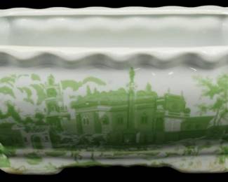 1024 - Green & White Transferware Planter (Description): Green and white transferware planter  featuring scenic landscape designs depicting  architectural buildings and trees. The  rectangular vessel has a scalloped rim edge,  twin scrolled handles on each end, and rests on decorative footed base. Measures 41/2  inches tall by 12 inches long by 6.5 inches  wide.