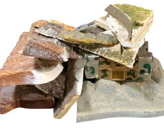 1706 - Lot HO Scale Train Track Terrain Pieces (Description): A lot of HO scale train track terrain pieces.  The collection includes various landscape  elements featuring rocky outcroppings, cliff  faces, and hillside sections with textured  surfaces simulating stone and earth. One piece incorporates a miniature building  facade resembling an Alpine or European-style  structure. The terrain pieces feature  painted details including greenery, moss  effects, and natural rock coloring in browns,