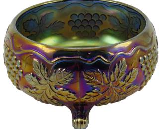 730 - Fenton Grape & Cable Cobalt Carnival Bowl (Description): Vintage Fenton Grape & Cable pattern carnival  glass bowl in cobalt blue. This striking  footed bowl features the classic grape and  leaf design in raised relief on the exterior,  with a coordinating grape motif on the interior. The iridescent finish displays  beautiful rainbow hues of purple, gold, and  green typical of fine carnival glass. The  bowl rests on three ball-shaped feet.  Measures 3 1/2" x 10".