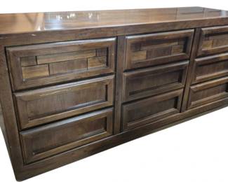 7621 - Dixie Mid-Century Brutalist 9 Drawer Dresser (Description): Mid-century modern walnut nine-drawer dresser  featuring a warm brown finish with rich wood  grain throughout. The dresser is arranged in  three columns of three drawers each, with  integrated horizontal drawer pulls creating a clean, streamlined appearance. The piece has  a plinth base and showcases quality  craftsmanship typical of the period. Measures  38 inches high by 66 inches wide by 19  inches deep.
