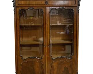 7771 - Ornately Carved Rosewood 2 Door Bookcase (Description): This elegant display cabinet features  ornately carved rococo-style crest rail with  floral motifs, decorative corner accents, and  scrolled cabriole feet. The two doors  feature glass upper panels with carved frames and beautifully figured wood lower panels.  Interior contains three adjustable shelves  for display or book storage. One drawer sits  beneath the shaped mirrored gallery top.  Measures 67 inches tall by 42 inches wide b