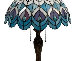 1509 - Tiffany Style Stained Glass Peacock Lamp 24" (Description): Tiffany style stained glass table lamp  featuring a peacock feather design. The dome  shade showcases an elegant pattern in shades  of blue, purple, and white art glass with  jeweled accents along the scalloped edge. The lamp rests on a decorative cast metal base  with an antique bronze finish and features  dual pull chain switches. Measures 24 inches  tall. As is electric/electronic/mechanical item. No