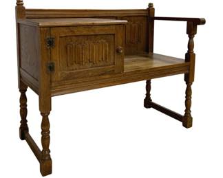 7752 - Vintage Oak Gossip Bench w/ Linenfold Panel (Description): Vintage oak gossip bench featuring a  single-seat design with carved linenfold  panel details on the cabinet door and back  panel. The piece showcases turned spindle  legs connected by stretchers, decorative finials, and a single armrest on the open  seat side. The cabinet section includes  ornate metal hinges and a wooden knob. A  charming example of English Tudor Revival  style furniture. Measures 30"x37"x18".