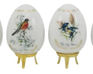 1092 - 6 Roger Tory Peterson Porcelain Eggs (Description): Set of six porcelain eggs by Roger Tory  Peterson, each featuring beautifully  hand-painted songbird illustrations with  floral accents and gilt detailing. The  collection includes various North American bird species including a cardinal, robin, and  bluebirds among flowering branches. Each egg  displays Peterson's signature and rests on  an ornate pierced brass stand. Measures 5  inches tall.