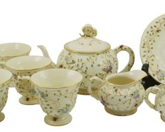 775 - Lenox Summer Enchantment 2006 Tea Set (Description): Lenox Summer Enchantment tea set from 2006.  This charming porcelain service features a  cream-colored ground adorned with delicate  hand-painted butterflies, ladybugs, and  trailing vine motifs with gold trim accents. The set includes a covered teapot with  butterfly finial, covered sugar bowl,  creamer, four teacups, and a saucer. Each  piece showcases the whimsical garden-inspired  pattern characteristic of this collectible