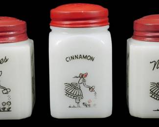 1152 - Vtg McKee Watering Can Lady 3 Spice Jars (Description): Vintage McKee Watering Can Lady spice jars,  set of three. Each white milk glass jar  features a charming black transfer design of  a girl with a watering can tending to  flowers. The jars are labeled Cloves, Cinnamon, and Nutmeg, and are fitted with red  painted metal shaker lids. Measures 3.5"  tall.