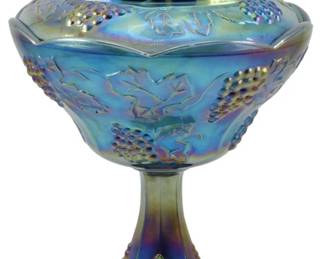 672 - Indiana Blue Harvest Grape Carnival Compote (Description): Vintage Indiana Blue Harvest Grape carnival  glass lidded compote. This striking piece  features the iconic Harvest Grape pattern  with raised grape clusters and leaf motifs  throughout the bowl and pedestal base. The glass displays a beautiful iridescent blue  carnival finish with purple and gold  highlights characteristic of this popular  pattern. The lid is topped with a dimensional  grape cluster finial. A lovely example of