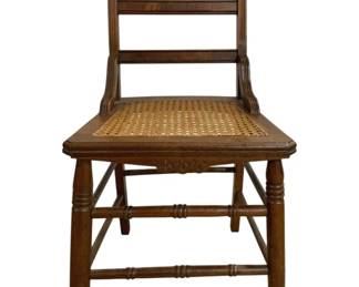 7664 - Walnut Vintage Cane Seat Side Chair (Description): Featuring a woven cane seat. The chair  displays Eastlake-style influences with a  carved crest rail featuring a stylized fan  motif and decorative incised details on the  seat apron. Constructed with turned front legs and stretchers for stability. The warm  wood finish shows character consistent with  age. Measures 33 inches high by 17 inches  wide by 17 inches deep.