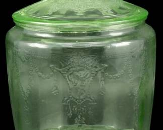 882 - Vtg 1930s Uranium Glass Biscuit Jar w/ Lid (Description): Vintage 1930s uranium glass biscuit jar with  matching lid. This Depression-era piece  features a beautiful green vaseline glass  with an embossed decorative pattern of draped  swags, garlands, and ornate medallion motifs on the body. The domed lid displays a  coordinating pressed pattern with a faceted  knob finial. The jar has a classic  cylindrical form with slightly indented  panels. Measures 7 1/2" x 10".