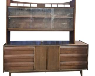 1421 - Lane First Edition 2 Part Hutch w/ Glass Top (Description): Lane two-part hutch featuring a glass-front  upper display cabinet with sliding doors and  interior shelving, topped with a distinctive  curved crest rail with spindle detailing. The  lower credenza base features six drawers with horizontal louvered fronts flanking a  central fitted drawer cabinet with ribbed  double doors. Mid-Century Modern walnut  construction with tapered splayed legs.  Measures 73 inches high by 74 inches wide by
