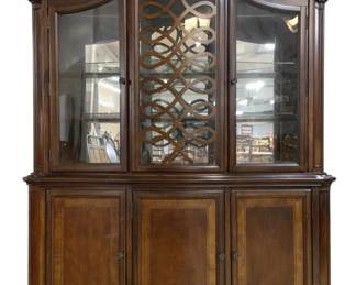 7729 - Ashley Millennium China Cabinet (Description): Traditional style china cabinet featuring an  arched bonnet top with decorative fretwork  overlay on the center glass door. The upper  display section has three glass-front doors  with interior lighting and glass shelves. The lower buffet base features four paneled  cabinet doors with burl wood inlay details.  Finished in a rich warm brown with serpentine  front design and bracket feet. Measures 88  inches high by 70 inches wide by 19 inches