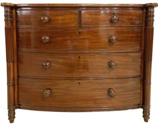 7747 - Sheraton Mahogany 2 Over 3 Drawer Chest (Description): Antique mahogany bow front chest of drawers  featuring a classic 2 over 3 drawer  configuration. The piece showcases beautiful  figured mahogany veneer with a warm, rich  patina. Flanked by elegant reeded columns with turned capitals and bases, the dresser  rests on turned feet. Each drawer is fitted  with original wooden knob pulls and  decorative escutcheons. The bow front design  and craftsmanship suggest English Regency or
