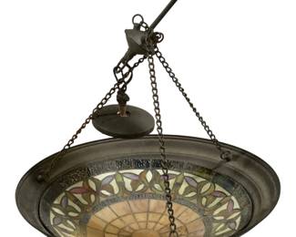 1652 - Stained Glass Hanging Light Fixture 18"x20" (Description): Stained glass hanging light fixture featuring  a domed shade with an amber-toned center  radiating outward in a sunburst pattern. The  decorative border showcases a repeating  floral or leaf motif in multicolored glass including shades of pink, lavender, green,  and cream, set within a textured clear glass  band. The fixture is mounted in a patinated  metal frame and suspended by chains from a  coordinating ceiling canopy with decorative