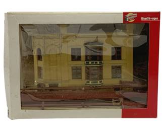 1058 - Walthers Cornerstone Built-Ups HO Scale Bldg (Description): Walthers Cornerstone Series Built-Ups HO  scale building, part of a 5-piece lot  described as HO Scale with best HO Train  Ideals. This pre-assembled model features a  Victorian-style yellow commercial building with ornate architectural details including  bay windows, decorative moldings, and an  arched entryway. The model comes in original  packaging with clear display window.