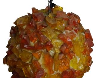 963 - Mid Century Chunky Lucite Swag Lamp 11" (Description): Mid Century chunky lucite swag lamp featuring  a spherical globe form composed of  irregularly shaped resin or acrylic chunks in  warm amber, orange, yellow, and tangerine  tones. The lamp hangs from a brass-toned chain and creates a striking textured  appearance characteristic of 1960s-70s  decorative lighting. Measures 11 inches in  diameter. Used as is electric/electronic/mechanical