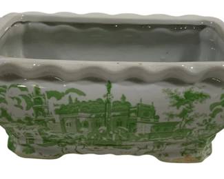 1529 - Green & White Transferware Ceramic Planter (Description): Green and white ceramic planter tub featuring  transferware-style scenic decoration  depicting architectural landscapes. The  rectangular vessel has a scalloped rim,  twisted rope handles on each side, and decorative footed base. Measures 12 inches by  6.5 inches by 5 inches.