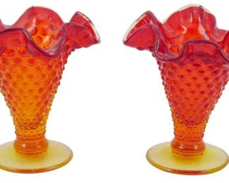 1000 - Pr Vtg Fenton Amberina Hobnail Vases 4" (Description): Pair of vintage Fenton amberina hobnail vases  measuring 4 inches tall. These charming  vases feature the classic hobnail texture  throughout the body with a beautiful gradient  coloring that transitions from deep ruby red at the ruffled crimped rim to warm amber  orange and yellow at the footed base. Each  vase has an elegant flared ruffled edge and  sits on a smooth round pedestal foot.