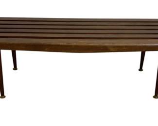 7615 - Mid-Century Modern Slatted Wood Coffee Table (Description): Mid-century modern slatted wood coffee table  featuring a long rectangular top composed of  parallel wooden slats in a warm walnut tone.  The table rests on four tapered legs with  brass ferrule feet, characteristic of the period's design aesthetic. Measures 14 inches  high by 60 inches wide by 19 inches deep.