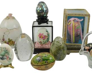769 - Assorted Vintage Decorative Painted Eggs (Description): A collection of assorted vintage painted eggs  in various styles and materials. The  grouping includes a porcelain egg trinket box  on gold-toned footed stand with floral and  lattice design, a frosted glass egg with applied floral decoration, a hand-painted egg  featuring a pastoral scene, a clear art  glass egg with controlled bubbles, an abalone  mosaic egg on black pedestal stand, a  cloisonné egg with landscape scene, a