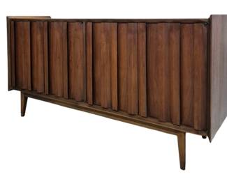 1407 - Lane Mid-Century First Edition Credenza (Description): Lane mid-century modern buffet featuring  distinctive vertical slat detailing on the  cabinet doors. The piece rests on angled  tapered legs characteristic of the MCM style.  Measures 31 inches high by 60 inches wide by 18 inches deep. Interior has a fitted  drawer.