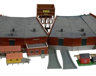 1702 - HO Scale Train Layout Buildings & Accessories (Description): Lot of HO scale train layout decorations  featuring a large dual roundhouse engine shed  with gray roofs and brick-red walls, a  coaling tower structure, and assorted smaller  buildings including a signal tower, small station buildings, and residential  structures. The lot also includes roadway  sections. Various pieces show weathering and  detailing typical of model railroad scenery.