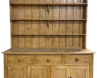 7789 - Antique Stripped Pine Welsh Dish Cupboard (Description): Antique two-part pine Welsh dish cupboard  featuring a traditional country farmhouse  design. The upper section displays three open  shelves with vertical plank backing, perfect  for displaying dishes and collectibles. The lower base cabinet offers three drawers with  turned wooden knobs above four paneled  cupboard doors providing ample enclosed  storage. The piece exhibits a warm, naturally  aged patina on the stripped pine wood.