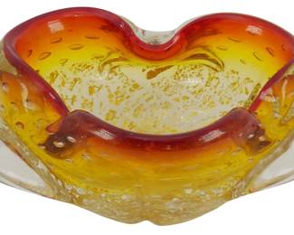 856 - Vintage Murano Amberina Glass Ashtray 2.5"x10" (Description): Vintage Amberina glass ashtray featuring a  beautiful gradient of deep red to golden  yellow coloring. The piece showcases a  decorative biomorphic shape with pinched  edges and a ruffled rim. The glass incorporates controlled bubble inclusions and  goldflecking throughout, characteristic of  mid-century art glass. Measures 2 1/2 inches  by 10 inches.