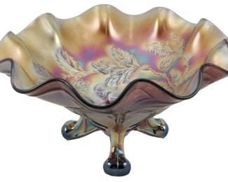 699 - Dugan Amethyst Panneled Cherries Carnival (Description): Vintage Dugan amethyst Panneled Cherries  pattern carnival glass footed bowl. This  beautiful piece features a ruffled rim with  an iridescent finish displaying golden,  purple, and pink hues. The bowl showcases the classic Panneled Cherries pattern with  raised cherry and leaf motifs. It rests on a  distinctive three-footed base with matching  iridescent carnival glass coloring. Measures  4 inches tall by 8 inches in diameter.