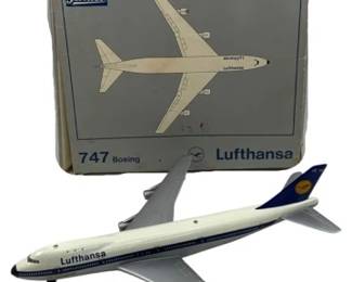 1215 - Schuco Lufthansa Boeing 747 Plane w/ Box (Description): Schuco Lufthansa Boeing 747 model airplane  with original box. The die-cast model  features the classic Lufthansa livery in  white with dark blue accents and the  airline's crane logo on the tail. The plane displays fine detailing typical of Schuco  collectible aircraft models. Includes the  original gray illustrated box marked "747  Boeing Lufthansa" with the Schuco logo. Plane  measures 11 x 9, has key.