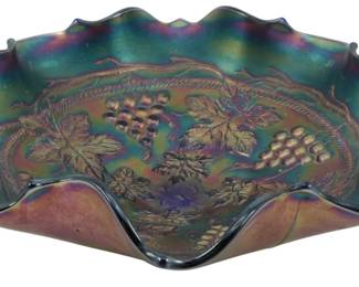 673 - Fenton Cobalt Blue Grape Cable Carnival Bowl (Description): Vintage Fenton Cobalt Blue Grape and Cable  Carnival Glass Bowl featuring an ornate  ruffled edge with a distinctive star-shaped  rim. The bowl showcases the classic Grape and  Cable pattern with raised grape clusters and vine leaves radiating from the center, all  exhibiting the characteristic iridescent  finish of carnival glass with beautiful  purple, gold, and green highlights against  the deep cobalt blue base. Measures 2" x