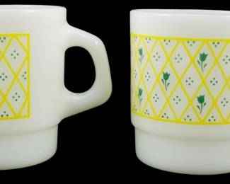 1132 - Pr Termocrisa Yellow Lattice w/ Green Flower (Description): Pair of Termocrisa milk glass mugs featuring  a yellow lattice pattern with green tulip  flowers and polka dot accents. These  stackable mugs showcase the classic Fire-King  style design popular in mid-century kitchenware. Measures 3.5" tall.